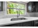 Modern kitchen sink with stainless steel faucet and white quartz countertop under window with lush backyard view at 7607 New York Ave, Hudson, FL 34667