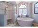 Luxurious bathroom with walk-in shower, standalone tub, and arched window providing natural light at 17544 Fairmeadow Dr, Tampa, FL 33647