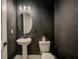 Elegant powder room features a pedestal sink, oval mirror, and a modern light fixture against a dark wall at 8717 Sanders Tree Loop, Wesley Chapel, FL 33545