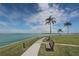 Picturesque waterfront view with a walkway, benches, palm trees, and a serene body of water under a blue sky at 1 Key Capri # 104E, Treasure Island, FL 33706