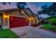 Two-car garage with a red door and landscaping at 957 Westwinds Blvd, Tarpon Springs, FL 34689