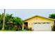 Charming yellow home featuring a two-car garage, lush landscaping, and great curb appeal at 1964 Arvis E Cir, Clearwater, FL 33764
