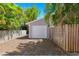 View of a detached one car garage with a white door surrounded by a wooden fence and greenery at 106 19Th Ave, St Pete Beach, FL 33706