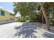 Large gravel parking area with mature trees and a glimpse of neighboring houses at 516 Gulf Blvd, Indian Rocks Beach, FL 33785