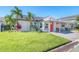 Cute bungalow with a bright orange door, lush lawn, and tropical landscaping at 142 Beach Ave, Redington Shores, FL 33708