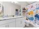 Well-lit bathroom with double sinks, white cabinets, and a shower/tub combo with a colorful shower curtain at 32924 Estate Garden Dr, Wesley Chapel, FL 33545