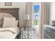 Detailed view of the bedroom with a mirrored nightstand, lamp, and view of the outside through sheer curtains at 32924 Estate Garden Dr, Wesley Chapel, FL 33545