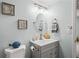 Clean bathroom with gray vanity, oval mirror, and coastal-themed art at 3232 Lake Pine E Way # H2, Tarpon Springs, FL 34688