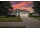 Charming single-story home featuring a well-manicured lawn, two-car garage, and a vibrant sunset at 2293 Dog Leg Ct, Brooksville, FL 34604