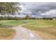 View of a community golf course with a concrete walking path, green fairway, trees, and cloudy skies at 2293 Dog Leg Ct, Brooksville, FL 34604