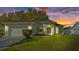 Evening view of house exterior with green color, two-car garage, and well-manicured lawn at 12739 Balsam Ave, Hudson, FL 34669