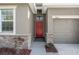 Close-up of a red front door with stone detailing and a well-kept landscape bed at 13822 Bee Tree Ct, Hudson, FL 34669