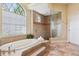Bright bathroom featuring a soaking tub with tiled surround, a glass-enclosed shower, and natural light from a large window at 20200 Lace Cascade Rd, Land O Lakes, FL 34637