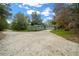 A gravel driveway leading to a home with two auxiliary buildings surrounded by verdant lawns and mature trees at 16325 Hibiscus Rd, Brooksville, FL 34601