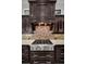 Close-up of the kitchen's stainless steel stove and custom range hood with tiled backsplash, and dark cabinets at 10309 Altrara Way, Trinity, FL 34655