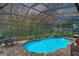 Bright blue swimming pool within a screened enclosure and brick patio, surrounded by lush greenery and garden decorations at 1031 Pomme De Pin Ln, New Port Richey, FL 34655
