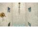 Close-up of a walk-in shower with mosaic tile floor, white tile walls, and bronze fixtures at 6613 Josie Ln, Hudson, FL 34667