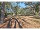 Tranquil backyard setting with mature trees casting dappled shadows on the grass and fallen leaves at 2454 Landover Blvd, Spring Hill, FL 34608