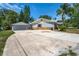 A single story home with a long driveway and attached garage is framed by lush trees and a clear blue sky at 5345 Carlton Rd, New Port Richey, FL 34652