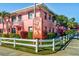 Exterior of a two-story pink condo building with tropical landscaping and white picket fence at 6800 Sunset Way # 1006, St Pete Beach, FL 33706