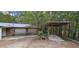 Rustic garage with covered carport and driveway in a wooded setting, offering storage and parking solutions at 11617 Duda Rd, Hudson, FL 34667