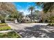 View of the community entrance with a guard house and a brick-paved road, surrounded by mature trees and green grass at 5383 Firethorn Pt, Spring Hill, FL 34609