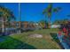 Beautifully landscaped backyard with pond view, lush green lawn, palm trees, and vibrant tropical plants at 494 Village Dr, Tarpon Springs, FL 34689