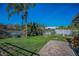 Landscaped backyard with lush green lawn, palm trees, brick patio, white fence, and serene pond view at 494 Village Dr, Tarpon Springs, FL 34689
