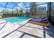 Screened-in pool with a waterfall feature, stone pavers, lounge chairs, and tropical landscaping at 2830 Dudley Ave, Odessa, FL 33556