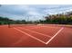 Outdoor tennis court with red surface, white lines, and a net under a cloudy sky at 370 Tall Oak Trl, Tarpon Springs, FL 34688