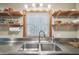 Stainless steel kitchen sink surrounded by open shelving and a window at 8721 Old Post Rd, Port Richey, FL 34668