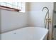 Modern white freestanding tub with gold hardware and a glass block window in the bathroom at 6393 Pinehurst Dr, Spring Hill, FL 34606