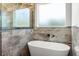 Modern bathroom featuring a freestanding tub under a window, complemented by elegant stone tile and a glass shower at 16043 Penn State Rd, Weeki Wachee, FL 34614