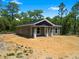 A charming one story home with a grey roof, pillars and front porch sits on a wooded lot under a sunny blue sky at 18082 Parakeet Rd, Brooksville, FL 34614