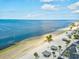 An aerial view of a beach with clear water, white sand, shelters, and lush tropical trees at 5557 Sea Forest Dr # 318, New Port Richey, FL 34652