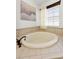 Elegant soaking tub with a tile surround, decorative art, and a bright window at 10623 Marsha Dr, New Port Richey, FL 34655