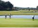 Scenic golf course featuring golfers on the green near a tranquil pond, set against a backdrop of lush green fields at 4831 Wakefield Ct, New Port Richey, FL 34655