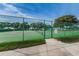 View of fenced tennis court and manicured landscaping on a sunny day with a blue sky at 9336 Cape Charles Ave, New Port Richey, FL 34655