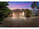 Exterior view of home at dusk, featuring a three-car garage, large brick driveway and lush, tropical landscaping at 7925 Calindra Ct, Trinity, FL 34655