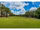 Lush green golf course featuring a red flag and mature trees set against a beautiful blue sky with clouds at 9636 Brookdale Dr, New Port Richey, FL 34655
