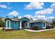 Blue home featuring a red door, lovely landscaping and a curved walkway leading to the entrance at 11379 Flower Ave, Weeki Wachee, FL 34613