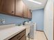 Functional laundry room with blue walls, wooden cabinets and a utility sink next to a white washer and dryer at 24104 Peppermill Dr, Brooksville, FL 34601