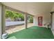 View of a covered patio with astroturf flooring, a red door, and a view of the yard and white fence at 3017 Aldoro Ave, Spring Hill, FL 34609