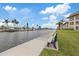 Scenic waterfront view with a bench, canal, lush grass, and palm trees under a clear blue sky at 4632 Marine Pkwy # 201, New Port Richey, FL 34652