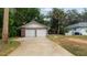 A two-car garage featuring brick accents and a long driveway bordered by mature trees and green space at 5417 Carlton Rd, New Port Richey, FL 34652