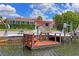 Charming waterfront property featuring a dock, a boat lift, lush landscaping, and a house with a red tile roof at 15635 Bertram Dr, Hudson, FL 34667