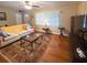 Bright living room with hardwood floors, plush sofa, ceiling fan, and natural light through large windows at 5406 Dartmouth Rd, New Port Richey, FL 34652