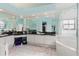 Well-lit bathroom with dual sink vanity, dark countertops, full mirrors, soaking tub, and a glass-enclosed shower at 9301 Tournament Dr, Hudson, FL 34667
