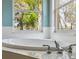 Luxurious bathtub with chrome fixtures, surrounded by tile and offering views of the beautiful greenery outside at 11631 Wayside Willow Ct, Hudson, FL 34667