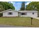 Single-story home with a well-kept lawn and mature trees under a beautiful blue sky, creating a serene setting at 6335 Kings Ct, New Port Richey, FL 34653